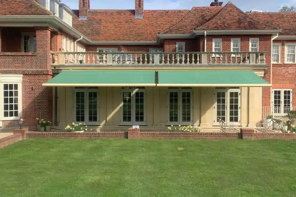 Twin Weinor awnings with green fabric fully extended over a patio of a red-brick period property