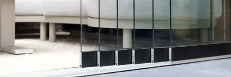 Frameless sliding glass doors partially opened inside a modern glass room.