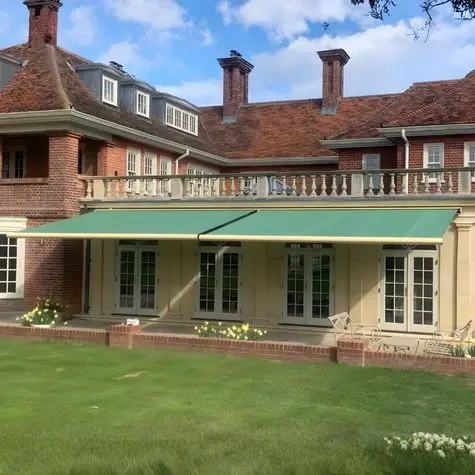 Green Weinor awning installation on luxury traditional home with manicured garden