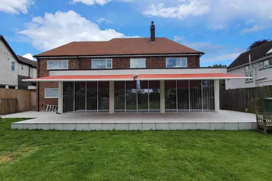 Dual Weinor Cassita II awnings in red extended over glass veranda on a modern brick home