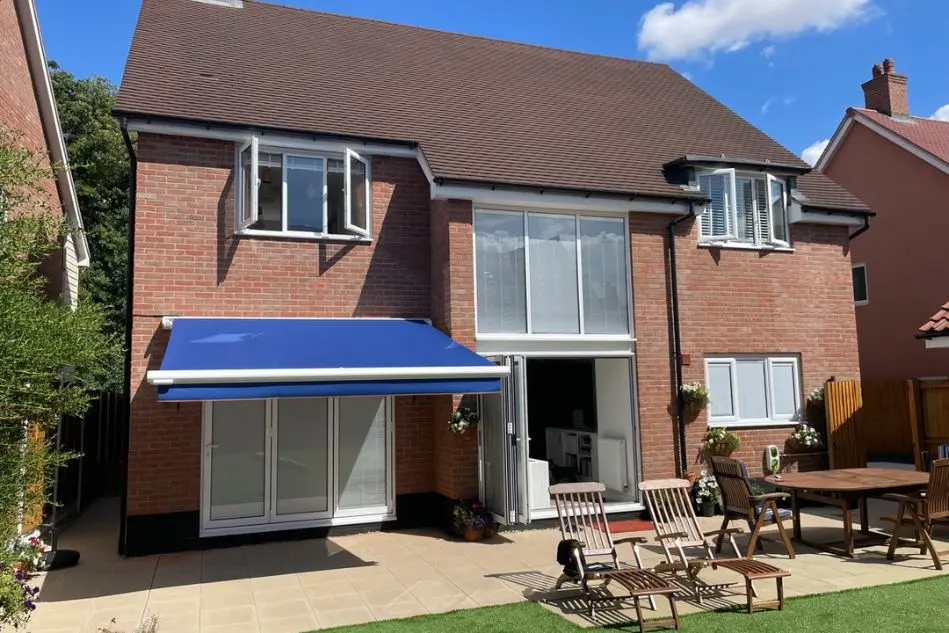 Full-width blue retractable awning installed on a brick house, shading a rear patio and outdoor seating area